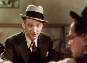 Movie still from “Doctor X” (1932), directed by Michael Curtiz – A man wearing a hat and a suit and tie; Close Up shot, Over the shoulder angle