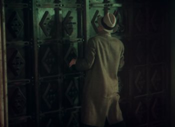 Movie still from “Doctor X” (1932), directed by Michael Curtiz – A man wearing a hat and a trench coat is standing in front of a wall; Medium shot, High angle