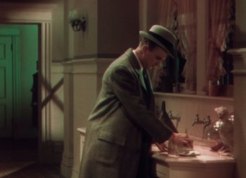 Movie still from “Doctor X” (1932), directed by Michael Curtiz – A man in a suit and a hat standing in front of a bathroom sink; Medium shot, High angle