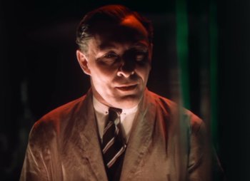 Movie still from “Doctor X” (1932), directed by Michael Curtiz – A man wearing a suit and tie standing in front of a green screen; Close Up shot, Low angle
