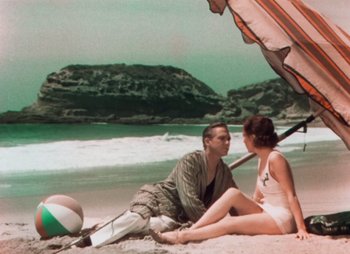 Movie still from “Doctor X” (1932), directed by Michael Curtiz – A man and a woman sitting under an umbrella on the beach; Wide shot, High angle