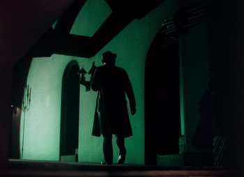 Movie still from “Doctor X” (1932), directed by Michael Curtiz – A man in a trench coat and hat walking in a dark room; Wide shot, Low angle