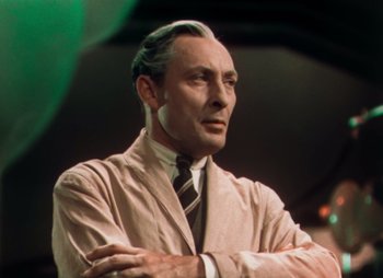 Movie still from “Doctor X” (1932), directed by Michael Curtiz – An older man in a suit and tie with his arms crossed; Medium shot, Low angle