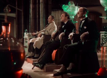 Movie still from “Doctor X” (1932), directed by Michael Curtiz – A group of men sitting in a row on a stage; Wide shot, Low angle