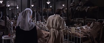 Movie still from “Doctor Zhivago” (1965), directed by David Lean – A man in a trench coat standing next to a bed; Medium shot, High angle