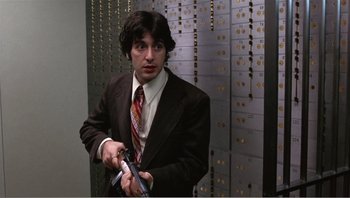 Movie still from “Dog Day Afternoon” (1975), directed by Sidney Lumet – A man in a suit and tie holding a gun in a room; Medium shot, Low angle