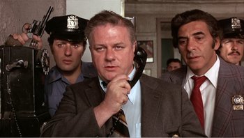 Movie still from “Dog Day Afternoon” (1975), directed by Sidney Lumet – A man holding a phone up to his ear while standing next to two other men; Medium shot, Low angle