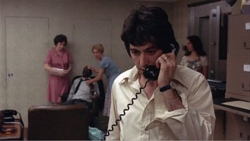 Movie still from “Dog Day Afternoon” (1975), directed by Sidney Lumet – A man talking on a phone in front of a group of people; Close Up shot, Over the shoulder angle