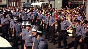 Movie still from “Dog Day Afternoon” (1975), directed by Sidney Lumet – A group of men in police uniforms marching in a parade; Wide shot, High angle