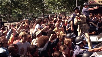 Movie still from “Dog Day Afternoon” (1975), directed by Sidney Lumet – A crowd of people sitting on the ground; Medium shot, High angle