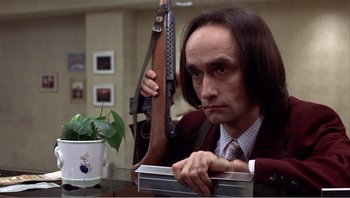 Movie still from “Dog Day Afternoon” (1975), directed by Sidney Lumet – A man sitting at a table holding a gun; Close Up shot, Low angle