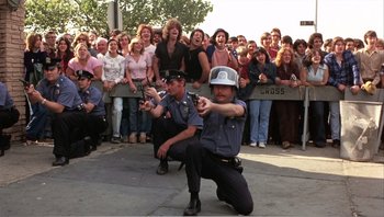 Movie still from “Dog Day Afternoon” (1975), directed by Sidney Lumet – A group of people standing around a crowd of people; Wide shot, High angle