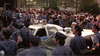Movie still from “Dog Day Afternoon” (1975), directed by Sidney Lumet – A group of police officers standing next to a police car; Wide shot, High angle