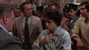 Movie still from “Dog Day Afternoon” (1975), directed by Sidney Lumet – A man adjusting his neck tie in front of a crowd; Medium shot, Over the shoulder angle