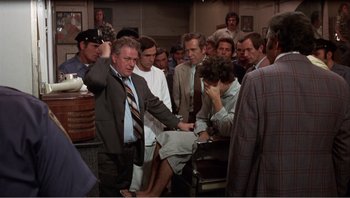 Movie still from “Dog Day Afternoon” (1975), directed by Sidney Lumet – A group of people gathered around a woman in front of a crowd; Wide shot, Over the shoulder angle