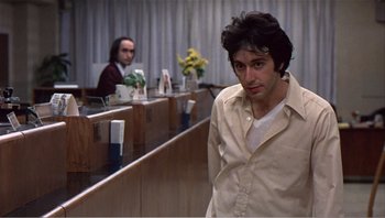 Movie still from “Dog Day Afternoon” (1975), directed by Sidney Lumet – A man standing in front of a counter in front of another man; Medium shot, Over the shoulder angle