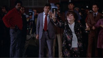 Movie still from “Dog Day Afternoon” (1975), directed by Sidney Lumet – An older woman in a black jacket and a red tie; Medium shot, Low angle