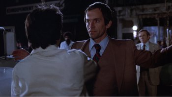 Movie still from “Dog Day Afternoon” (1975), directed by Sidney Lumet – A man wearing a suit and tie standing next to another man; Medium shot, Over the shoulder angle