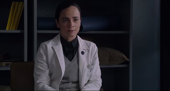 Movie still from “The New Mutants” (2020), directed by Josh Boone – A woman in a white lab coat sitting in front of a bookshelf; Medium shot, Low angle