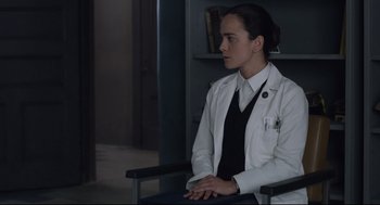 Movie still from “The New Mutants” (2020), directed by Josh Boone – A woman in a white lab coat sitting in a chair in a room; Medium shot, Over the shoulder angle