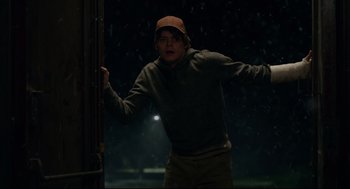Movie still from “The New Mutants” (2020), directed by Josh Boone – A young man in a brown hat is standing in the rain; Medium shot, Over the shoulder angle
