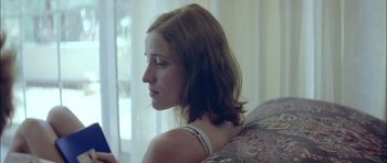 Movie still from “Dogtooth” (2009), directed by Yorgos Lanthimos – A woman sitting on top of a couch looking out a window; Close Up shot, Low angle