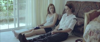 Movie still from “Dogtooth” (2009), directed by Yorgos Lanthimos – Two women sitting on a chair in front of each other; Medium shot, High angle