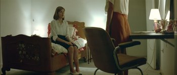 Movie still from “Dogtooth” (2009), directed by Yorgos Lanthimos – A woman sitting on a couch in front of another woman; Medium shot, Over the shoulder angle