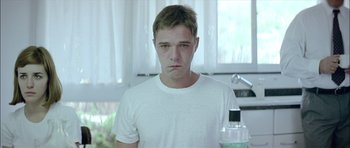 Movie still from “Dogtooth” (2009), directed by Yorgos Lanthimos – A man in a white t - shirt is holding a bottle; Medium shot, Low angle