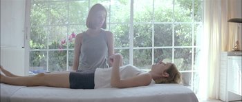 Movie still from “Dogtooth” (2009), directed by Yorgos Lanthimos – A woman sitting next to a woman laying on a bed; Medium shot, Over the shoulder angle