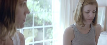 Movie still from “Dogtooth” (2009), directed by Yorgos Lanthimos – A woman standing in front of a large window; Close Up shot, Over the shoulder angle