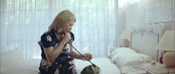 Movie still from “Dogtooth” (2009), directed by Yorgos Lanthimos – A woman is talking on the phone in a bedroom; Medium shot, High angle