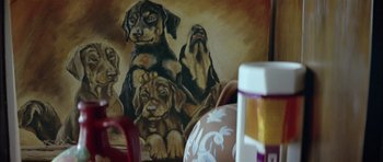 Movie still from “Dogtooth” (2009), directed by Yorgos Lanthimos – A painting of dogs sitting on a table; Extreme Close Up shot, High angle