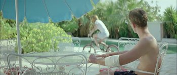 Movie still from “Dogtooth” (2009), directed by Yorgos Lanthimos – Two people sitting at a table with a bicycle in front of them; Medium shot, Over the shoulder angle