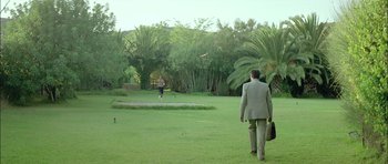 Movie still from “Dogtooth” (2009), directed by Yorgos Lanthimos – Two men in suits are walking in a park; Extreme Wide shot, Over the shoulder angle