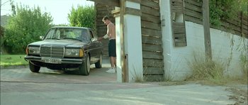 Movie still from “Dogtooth” (2009), directed by Yorgos Lanthimos – A man standing in front of a black car; Wide shot, Low angle
