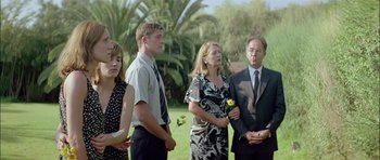Movie still from “Dogtooth” (2009), directed by Yorgos Lanthimos – A group of people standing next to each other in a field; Medium shot, Over the shoulder angle