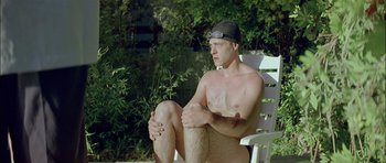 Movie still from “Dogtooth” (2009), directed by Yorgos Lanthimos – A man sitting on top of a white chair in the grass; Medium shot, Low angle