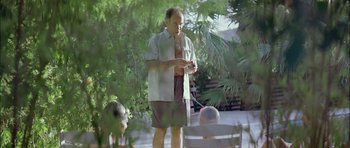 Movie still from “Dogtooth” (2009), directed by Yorgos Lanthimos – A man standing in a yard holding a cell phone; Medium shot, Over the shoulder angle