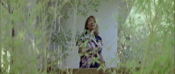 Movie still from “Dogtooth” (2009), directed by Yorgos Lanthimos – A woman standing in front of some bushes; Medium shot, Low angle