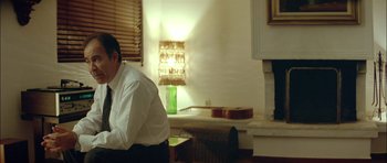 Movie still from “Dogtooth” (2009), directed by Yorgos Lanthimos – A man sitting in front of a lamp in a living room; Medium shot, Low angle