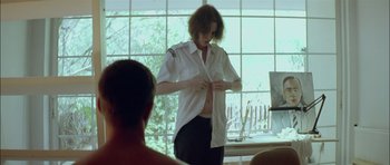 Movie still from “Dogtooth” (2009), directed by Yorgos Lanthimos – A woman in a white shirt is putting on a white shirt; Medium shot, Over the shoulder angle