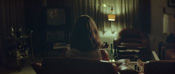Movie still from “Dogtooth” (2009), directed by Yorgos Lanthimos – A woman sitting on a couch in front of a window; Medium shot, Over the shoulder angle