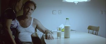 Movie still from “Dogtooth” (2009), directed by Yorgos Lanthimos – A woman sitting at a table with a glass of milk; Medium shot, Over the shoulder angle