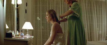 Movie still from “Dogtooth” (2009), directed by Yorgos Lanthimos – A young girl sitting in front of a mirror while a woman stands next to her; Medium shot, Over the shoulder angle