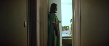 Movie still from “Dogtooth” (2009), directed by Yorgos Lanthimos – A woman in a green dress standing in front of a window; Medium shot, Over the shoulder angle