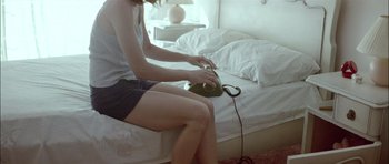 Movie still from “Dogtooth” (2009), directed by Yorgos Lanthimos – A person sitting on a bed with a phone; Medium shot, High angle