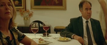 Movie still from “Dogtooth” (2009), directed by Yorgos Lanthimos – Two people sitting at a dinner table with wine glasses; Medium shot, Over the shoulder angle