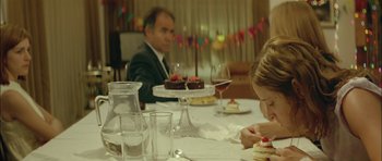 Movie still from “Dogtooth” (2009), directed by Yorgos Lanthimos – A woman sitting at a table with a cake; Medium shot, Over the shoulder angle
