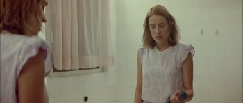 Movie still from “Dogtooth” (2009), directed by Yorgos Lanthimos – A young girl is standing in a bathroom; Medium shot, Over the shoulder angle
